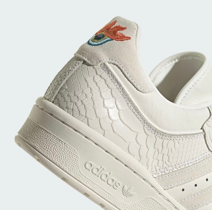 Close-up shot of a white Adidas sneaker featuring a scale-like pattern on the side and an embroidered logo on the heel.