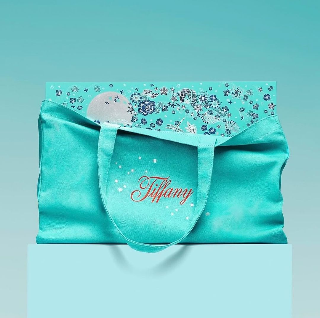 Turquoise Tiffany & Co. gift bag with floral-patterned box on a light blue cube against a blue background, showcasing luxury branding.