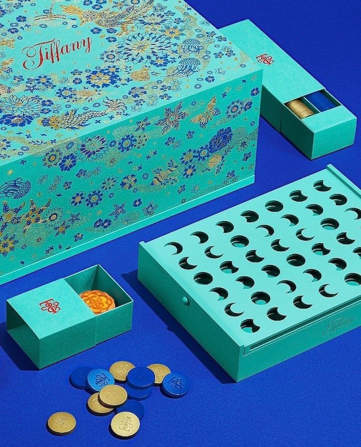 Elevated shot of Tiffany & Co. board game set featuring turquoise boxes with gold/blue details against a matching vibrant blue background.