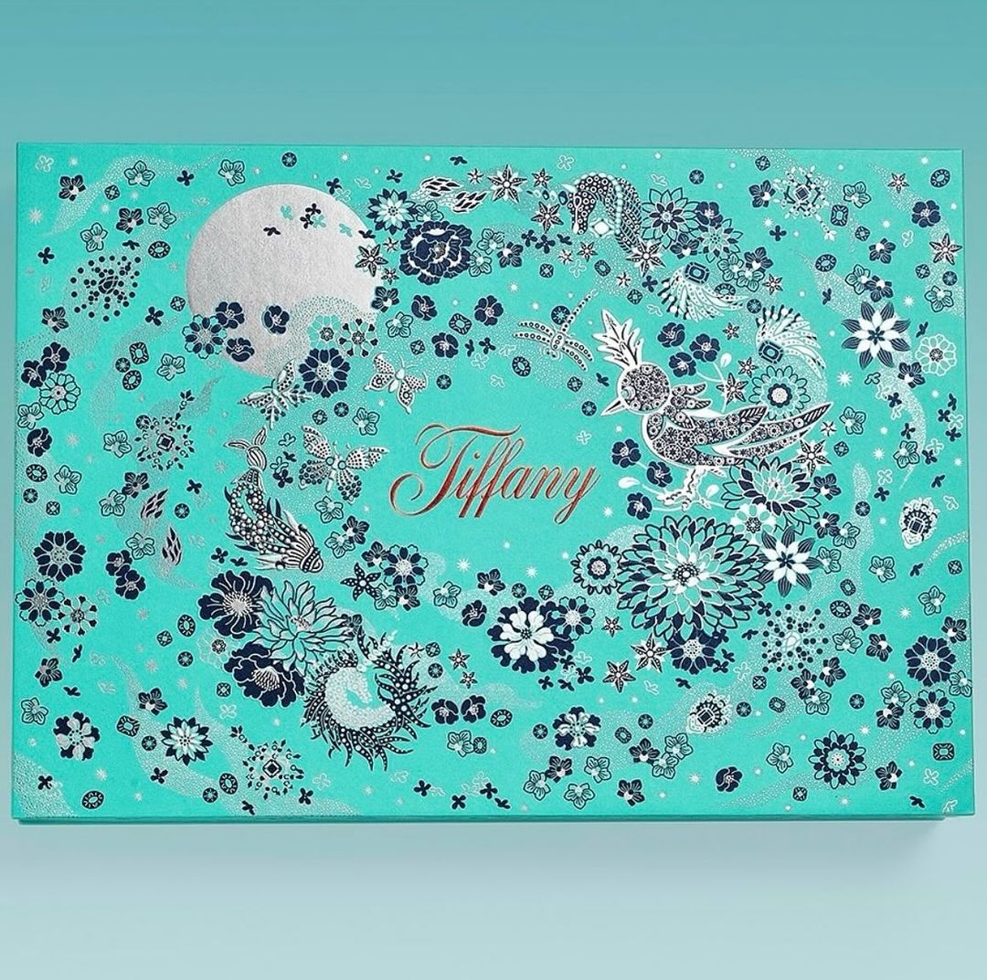 Turquoise Tiffany & Co. box adorned with silver floral and bird designs, a large moon, and the brand's gold cursive logo.