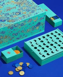 Turquoise Tiffany packaging boxes with floral patterns and a game board with blue and gold tokens on a blue surface.