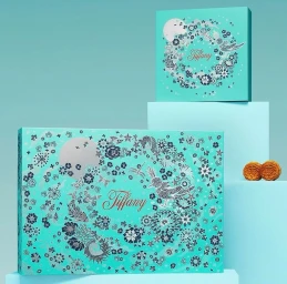 Turquoise Tiffany boxes featuring intricate silver floral illustrations and typography, arranged on tiered platforms with two mooncakes.