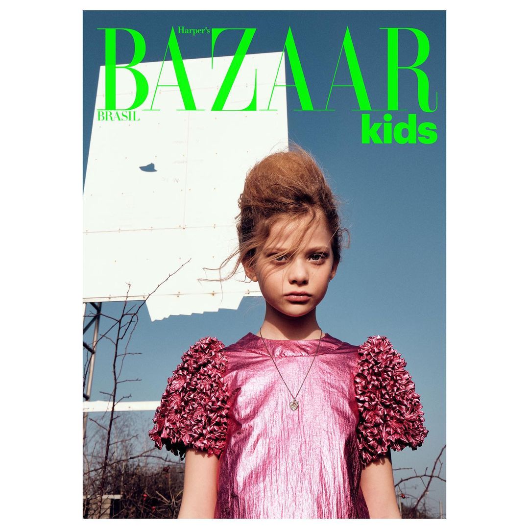 Magazine cover featuring a young female child model wearing a pink dress with frilled sleeves, posing against a blue sky.