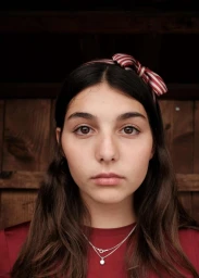 Portrait of young woman with dark hair wearing a striped bow and red top against a wood background