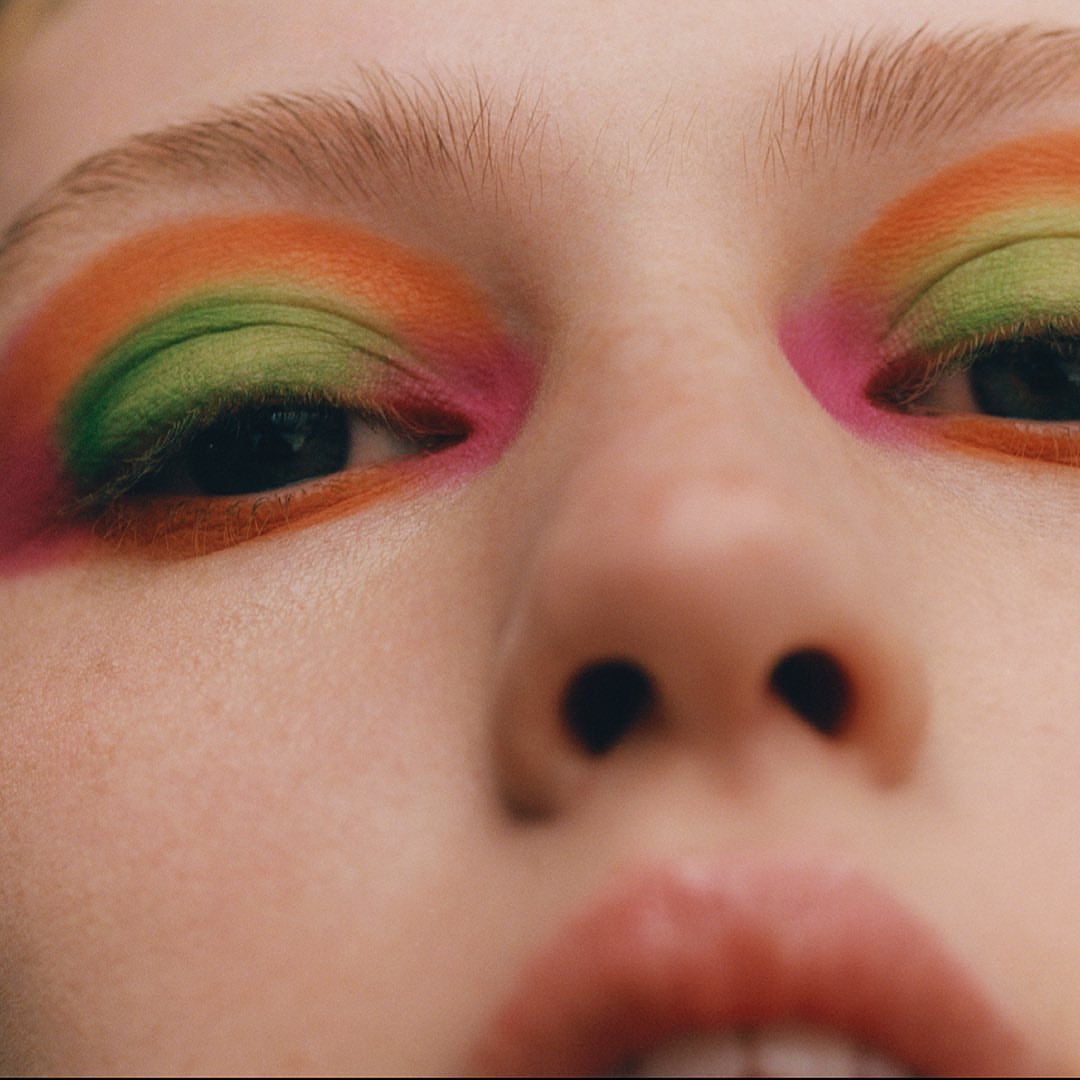 Extreme close-up portrait of a model with vibrant orange, green, and pink eyeshadow by Felicity Ingram
