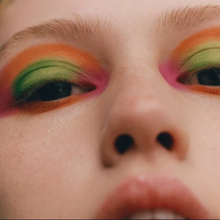 Extreme close-up portrait of a model with vibrant orange, green, and pink eyeshadow by Felicity Ingram