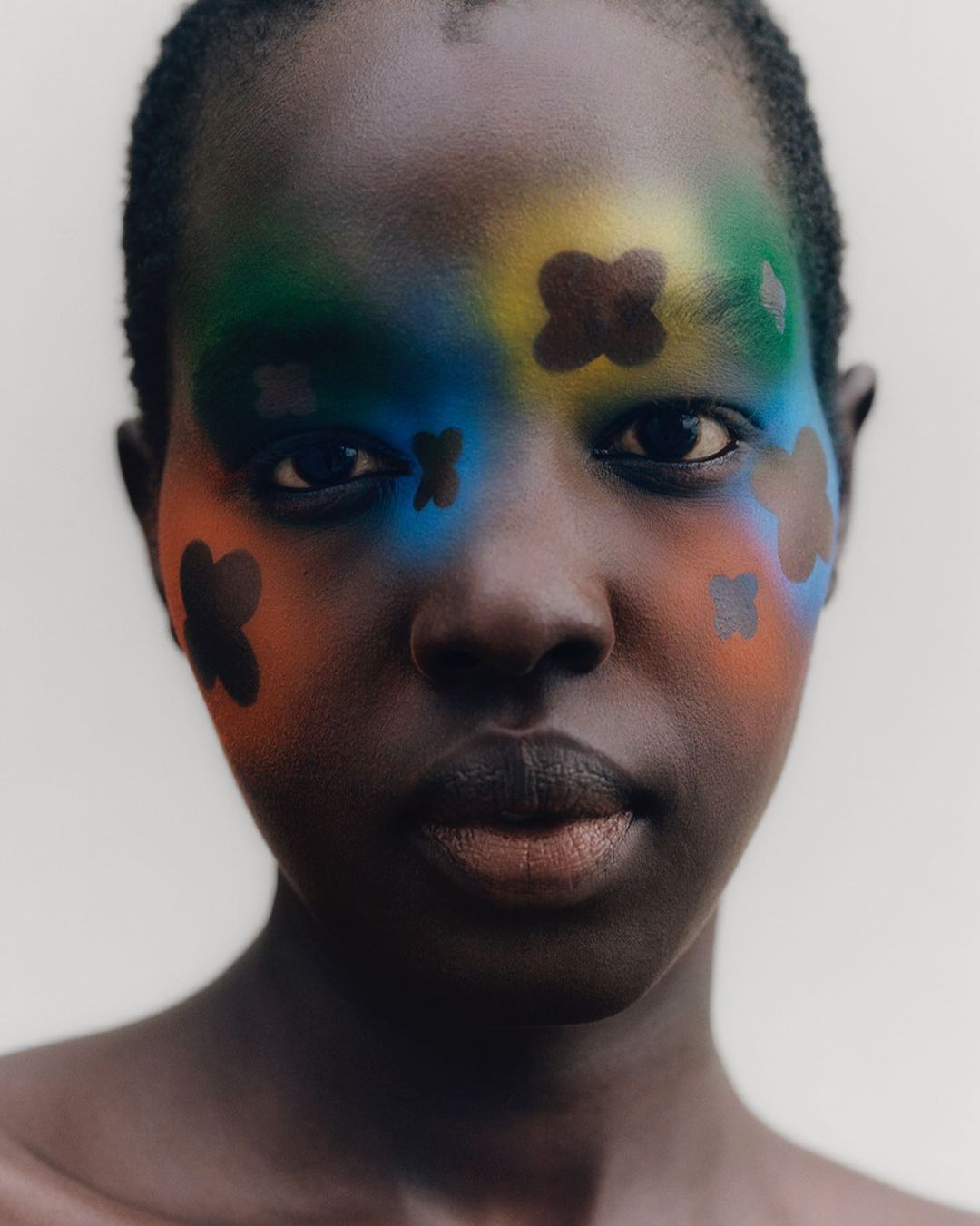 Striking portrait of an African woman with dark skin, adorned with vibrant face paint in shades of blue, green, yellow, and orange.