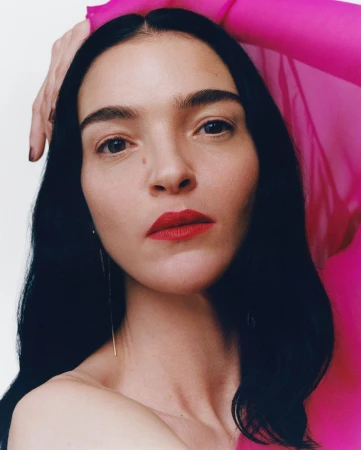 Close-up portrait of a woman with dark hair wearing vibrant pink sheer fabric against a plain white background