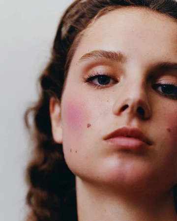 Close-up beauty portrait of a young woman with pink blush and prominent moles by photographer Felicity Ingram