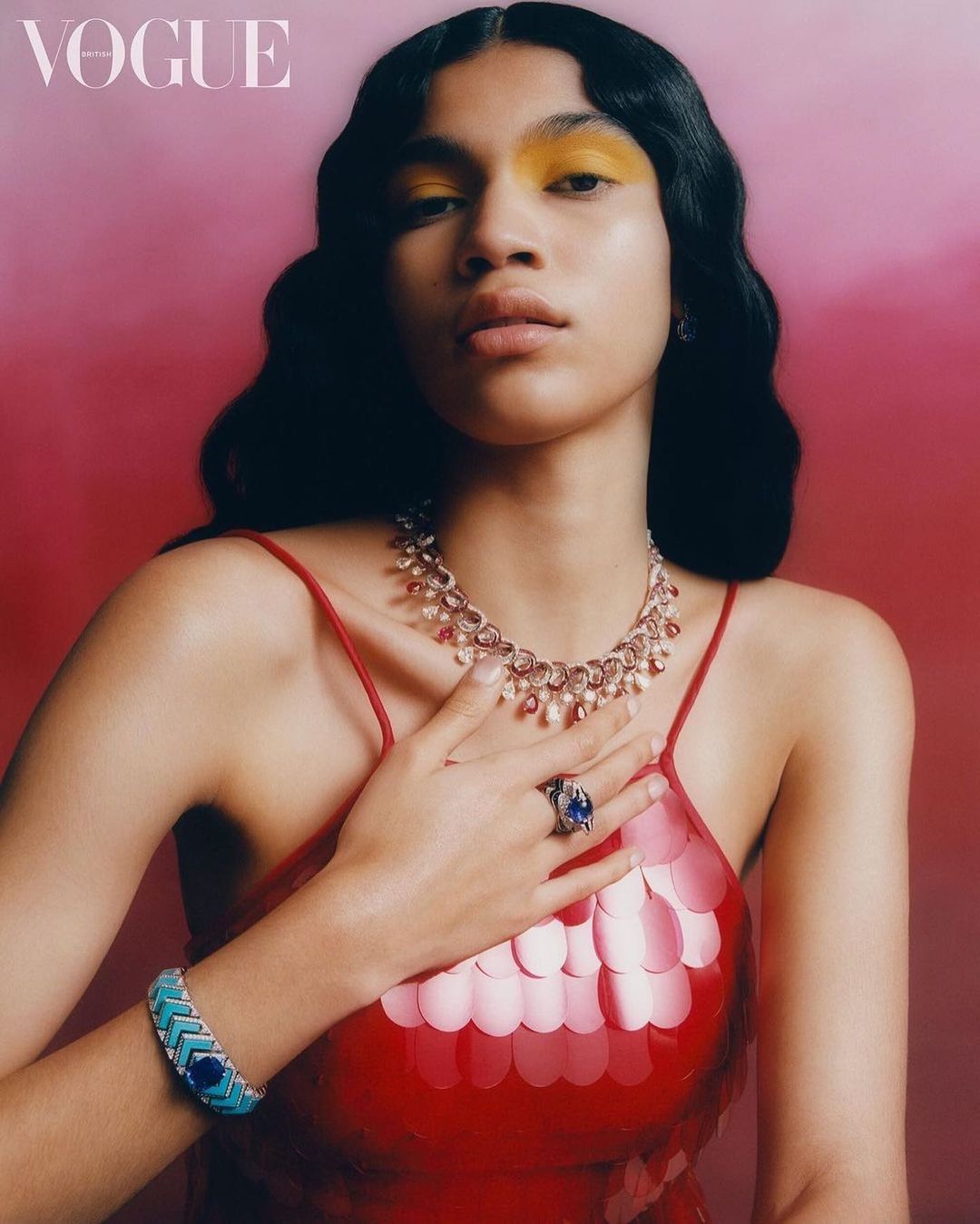 Young woman in a red sequin dress and yellow eyeshadow poses indoors with a necklace, bracelet, and ring in a studio shot.