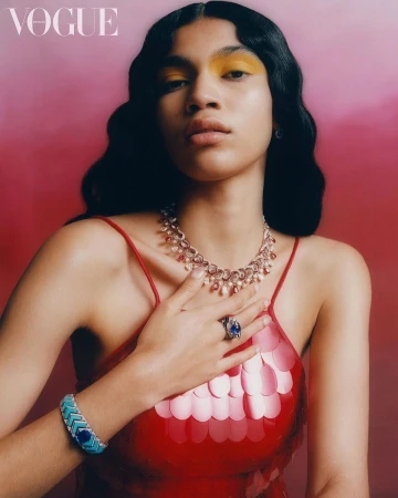 Young woman in a red sequin dress and yellow eyeshadow poses indoors with a necklace, bracelet, and ring in a studio shot.