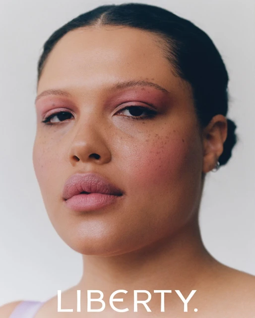 Close-up portrait of an adult female model with pink eye shadow and lipstick against a clean white backdrop, showcasing beauty and makeup.