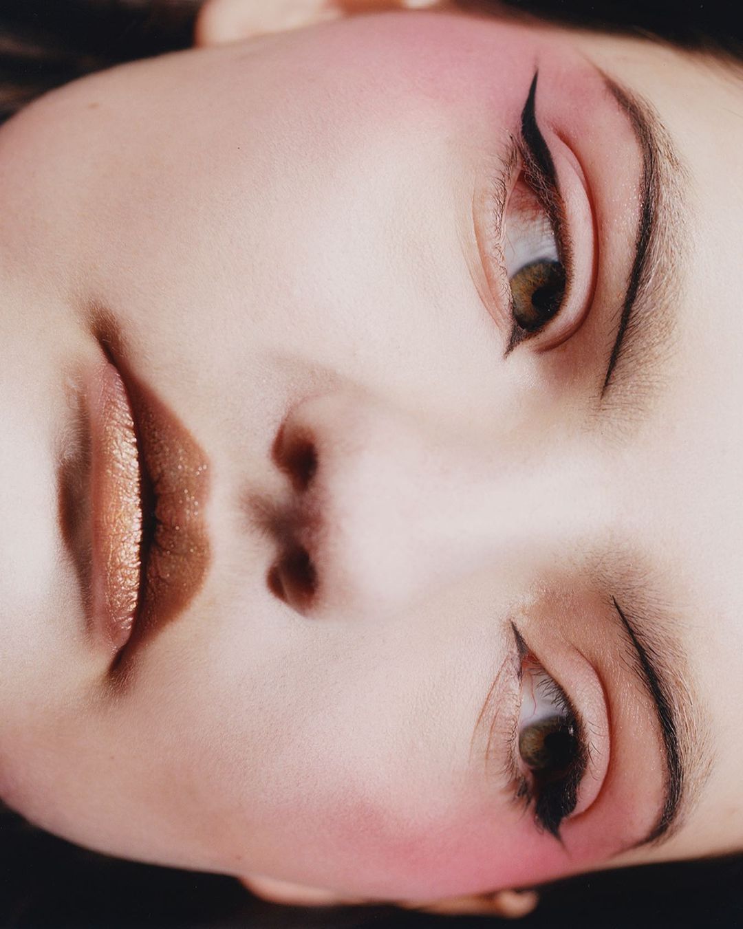 Close-up beauty portrait of a woman with dramatic black winged eyeliner and shimmering bronze lipstick shot by Felicity Ingram