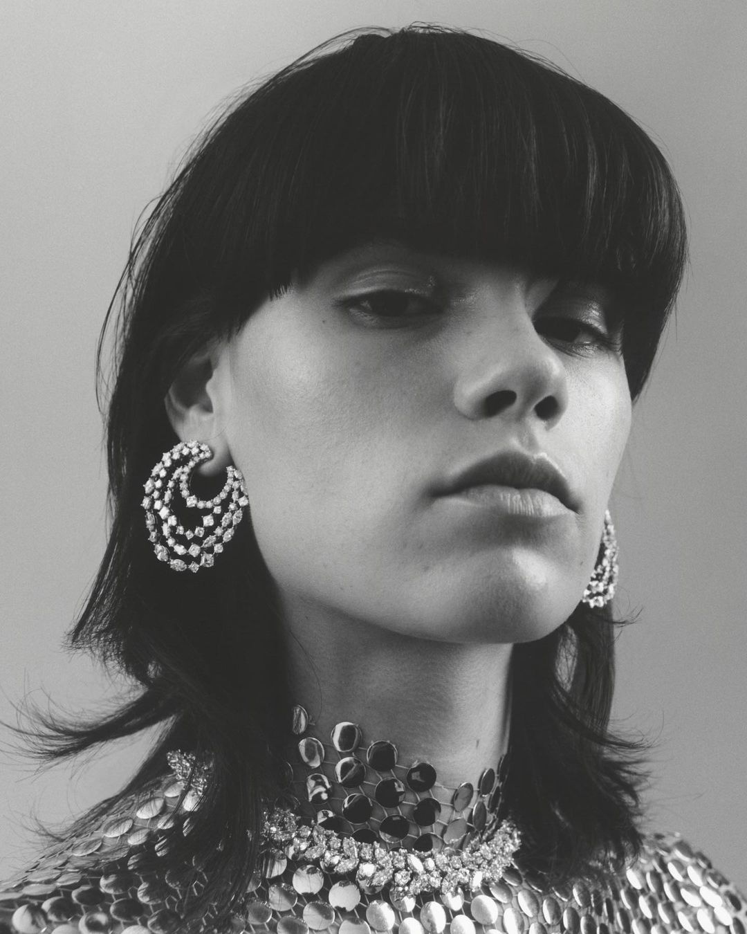 Close-up black and white portrait of a woman with short black hair wearing large silver earrings and a silver necklace. Fashion shot.
