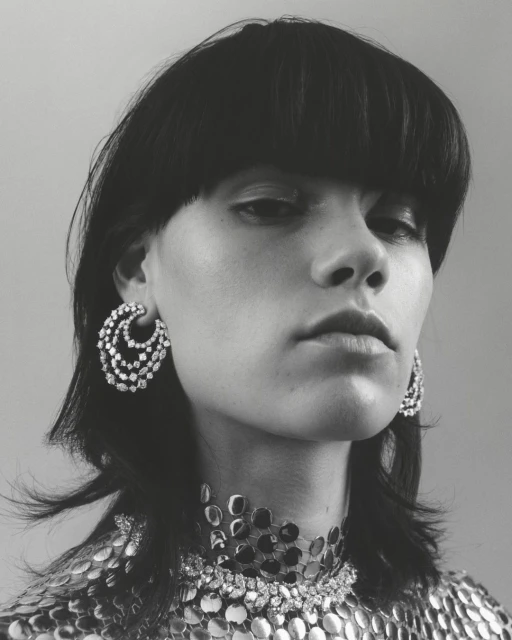 Close-up black and white portrait of a woman with short black hair wearing large silver earrings and a silver necklace. Fashion shot.