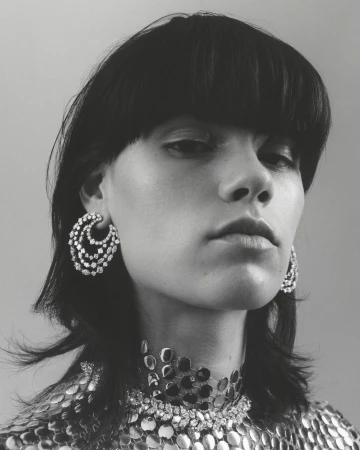Close-up black and white portrait of a woman with short black hair wearing large silver earrings and a silver necklace. Fashion shot.
