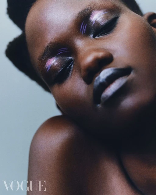 Close-up fashion shot of a dark-skinned woman with creative white and purple makeup, eyes closed, against a light blue background.