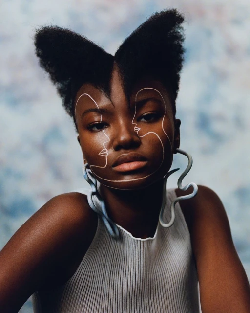 Portrait of a woman with dark skin and an artistic, abstract white face paint design. She wears a white top against a soft, blurred background.