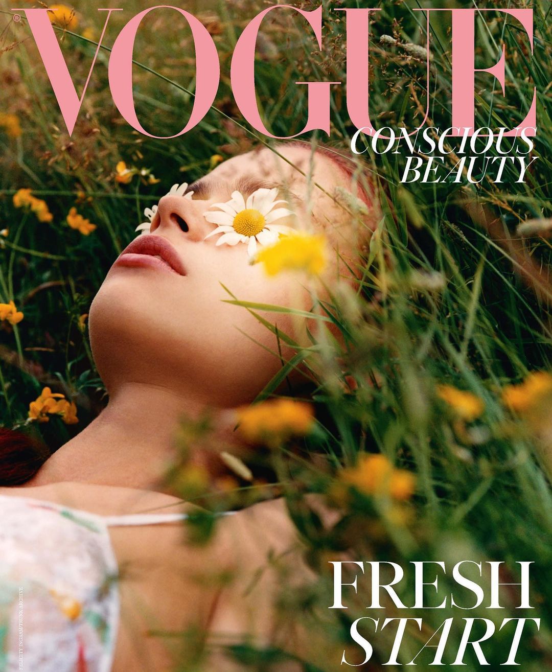 Vogue cover featuring a woman lying in a field of green grass and yellow flowers, with daisies covering her eyes.