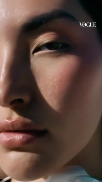 Close-up of an Asian woman's face with makeup and glossy lips, highlighting skincare in bright, natural lighting with Vogue logo.