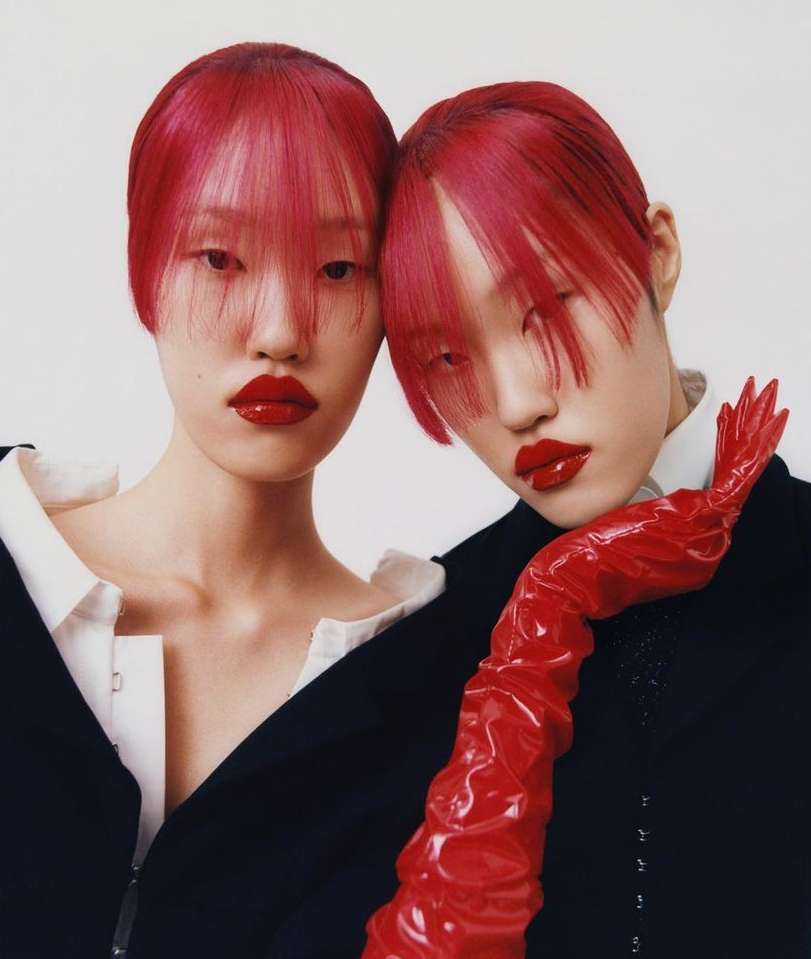 Striking editorial shot featuring two Asian women with vibrant red hair, glossy red lips, and fashion-forward black blazers against a white backdrop.
