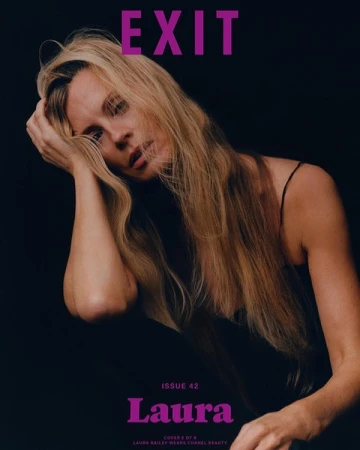Portrait of a blonde woman with long hair holding her hand to her head against a dark background, photographed by Felicity Ingram.