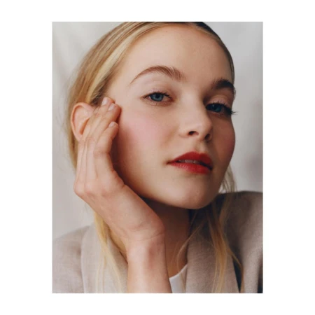 Close up portrait of a woman with blond hair touching her face wearing a beige jacket photographed by Felicity Ingram.