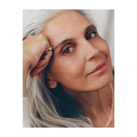 Close-up portrait of an older woman with long silver hair and a gold ring on her hand by Felicity Ingram