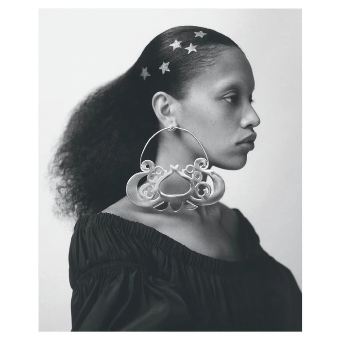 Profile portrait of a woman wearing a large sculptural silver earring and star decorations in her dark hair.