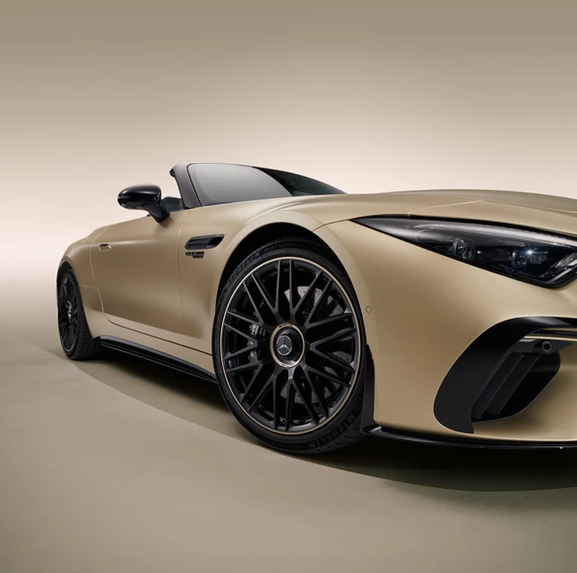 Studio shot of a gold Mercedes-Benz roadster car, showcasing its sleek design, black rims, and luxurious details against a neutral backdrop.