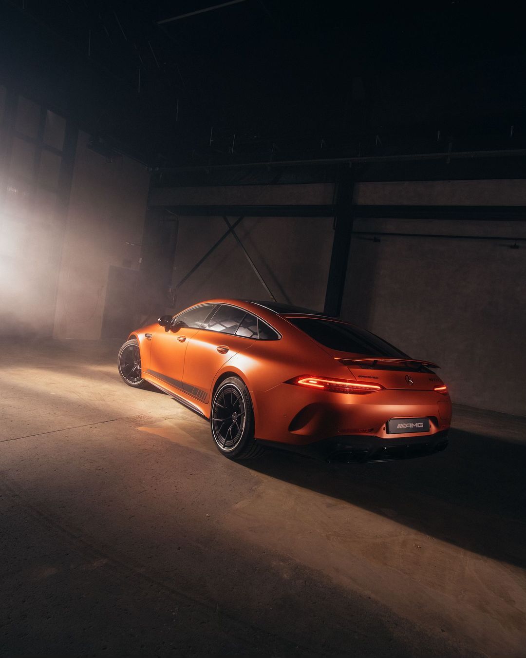 Luxury copper-colored sedan in a dimly lit studio, illuminated by a single light source. Automotive photography showcases elegant design.