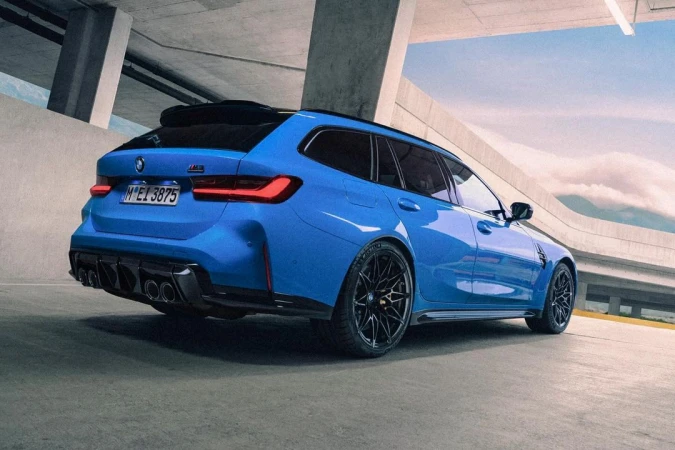 Rear view of a blue BMW M3 Touring car with black wheels parked on a concrete surface, showcasing its design and spacious interior.