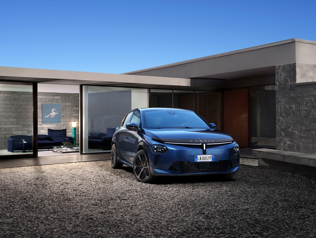 Blue Lancia Ypsilon car parked outside a modern house with gravel. Clear sky, luxury vehicle and architectural design blend seamlessly.