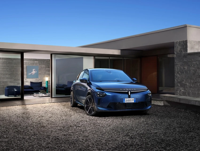 Blue Lancia Ypsilon car parked outside a modern house with gravel. Clear sky, luxury vehicle and architectural design blend seamlessly.