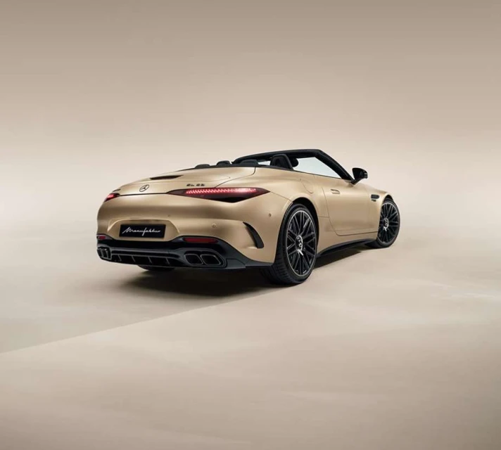 Rear view of a gold metallic Mercedes-Benz AMG SL roadster convertible parked in a photo studio, showcasing its elegant design.