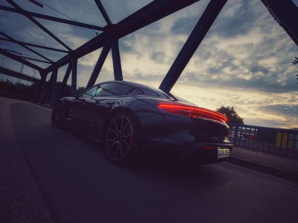 Sleek black Porsche Taycan parked on a bridge against a cloudy sky, showcasing its taillight design and elegant silhouette.