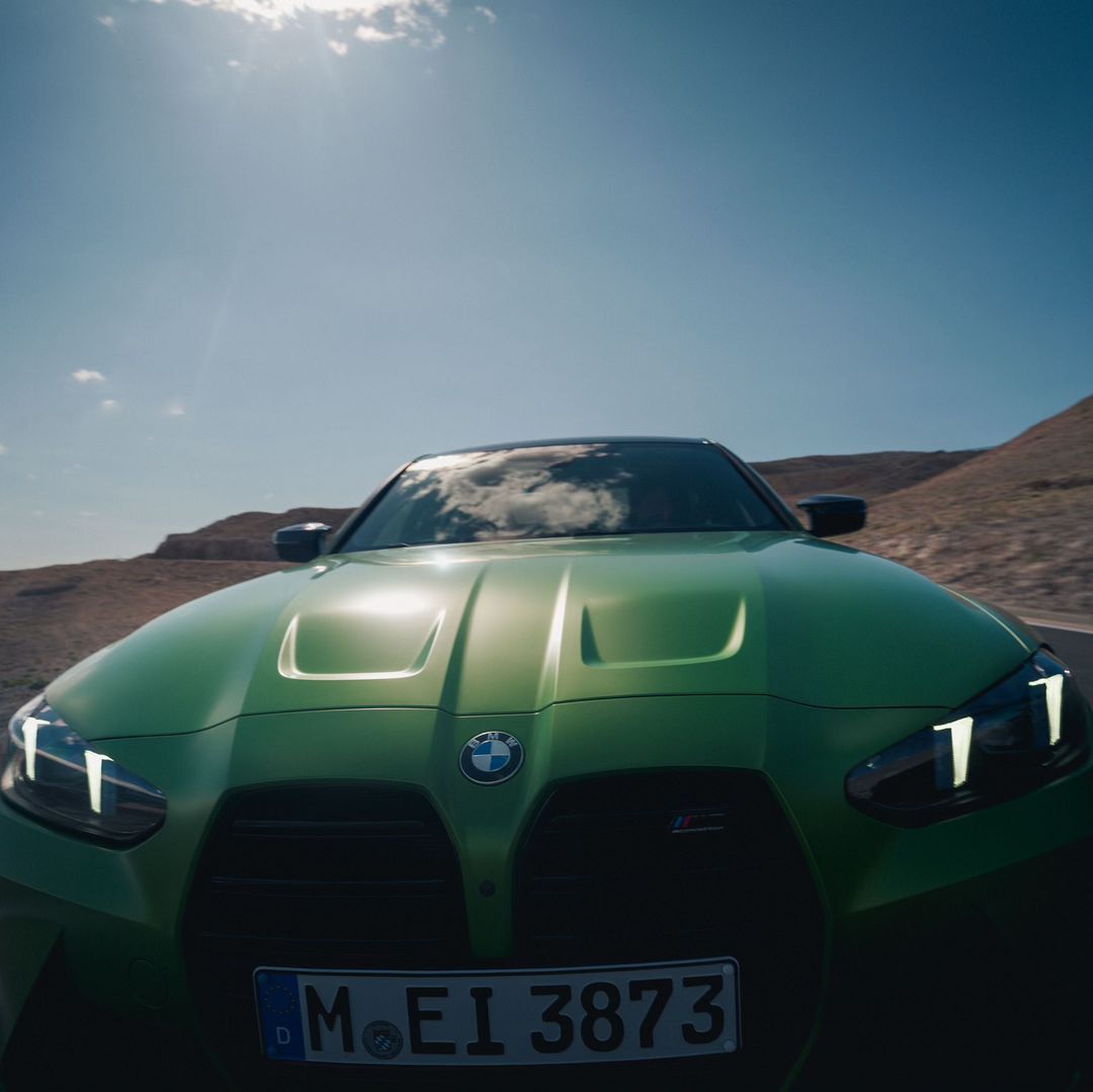 Lime green BMW sports car parked in a desert landscape with blue sky and bright sunlight casting shadows in this outdoor shot.