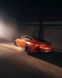Matte orange luxury sports sedan parked inside an industrial concrete garage with moody atmospheric lighting