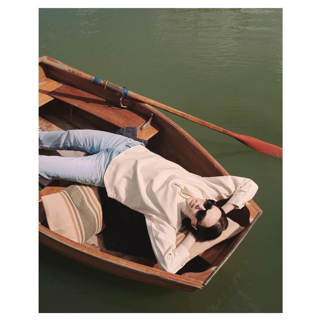 Woman in boat on water. Adult female reclining in a wooden rowboat with an oar, in outdoor scene with natural light and green water.