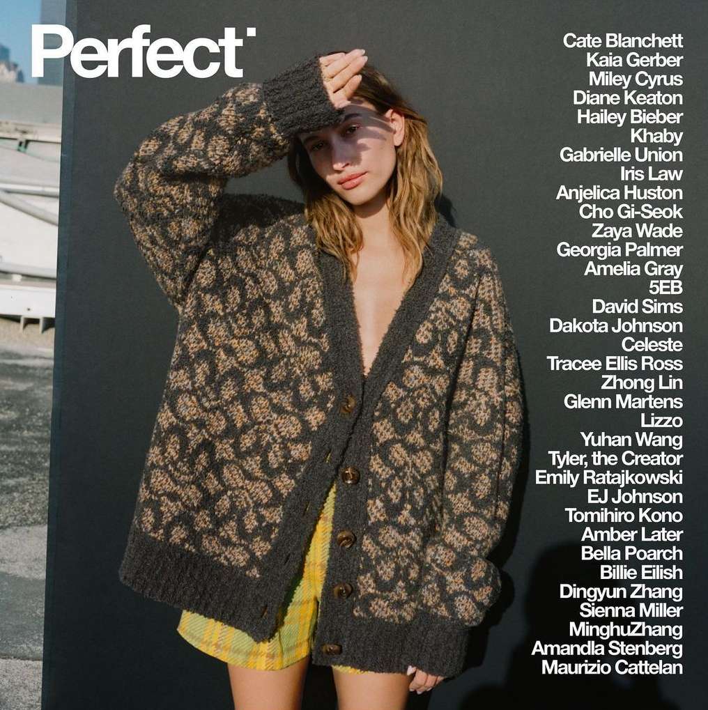Hailey Bieber wearing a patterned cardigan and raising a hand to her forehead against a dark backdrop with white text.