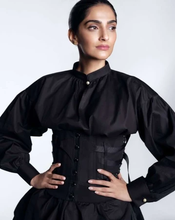 Portrait of Sonam Kapoor wearing a black buttoned blouse with a structured corset belt against white