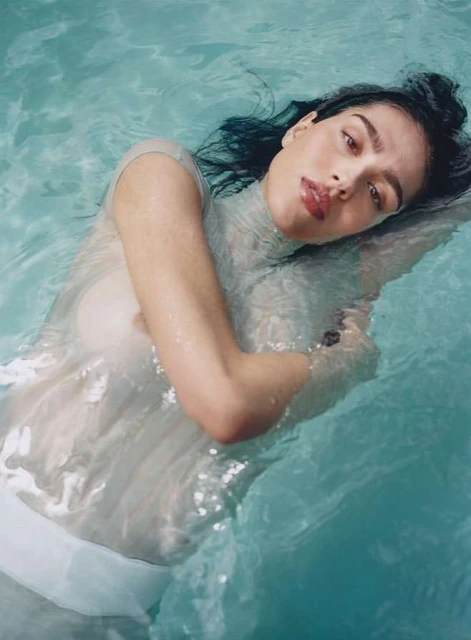 Portrait of a woman floating in water wearing a sheer white top. Close up of her face, shoulders and torso. The water is light blue.