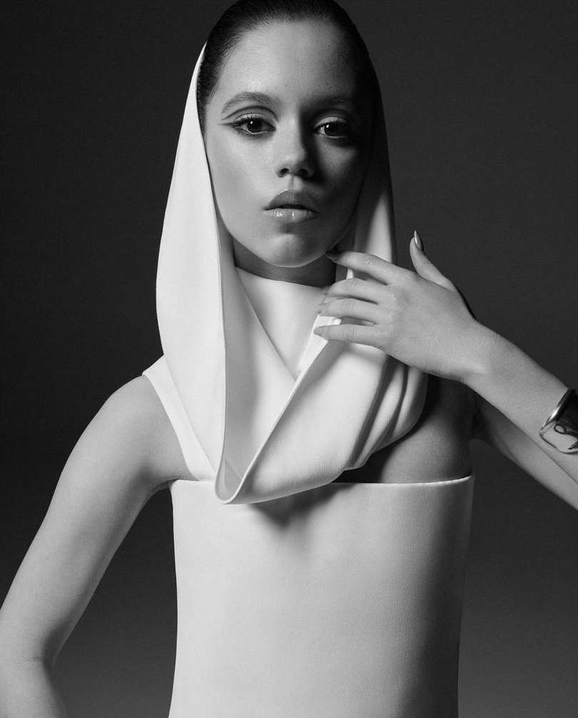Monochromatic fashion portrait of a woman in a sleek white dress and matching head covering against a dark studio backdrop.