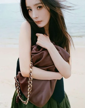 East Asian woman holding a brown leather shoulder bag on a sandy beach in London