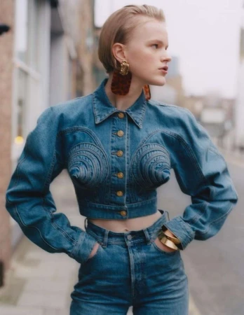 Model with short hair wearing a sculpted denim jacket and high-waisted jeans, standing on a London street.