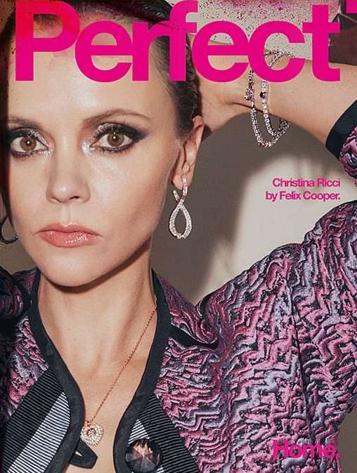 Close-up portrait of adult female Christina Ricci on a magazine cover with pink graphic text. She is wearing jeweled earrings and necklace.
