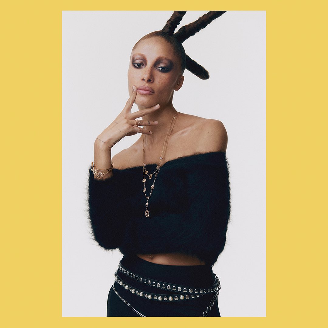 Portrait of a woman with updo wearing a black off-the-shoulder sweater and rhinestone belt against a white background.