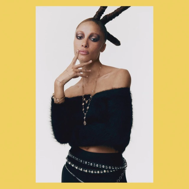 Portrait of a woman with updo wearing a black off-the-shoulder sweater and rhinestone belt against a white background.