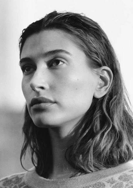 Portrait of a young adult female with wavy hair, wearing a sweater, against a neutral background in a black and white photograph.