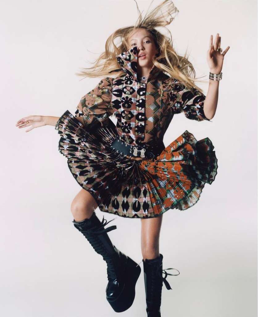Model jumping in the air wearing a patterned printed dress and black platform boots against a white background.